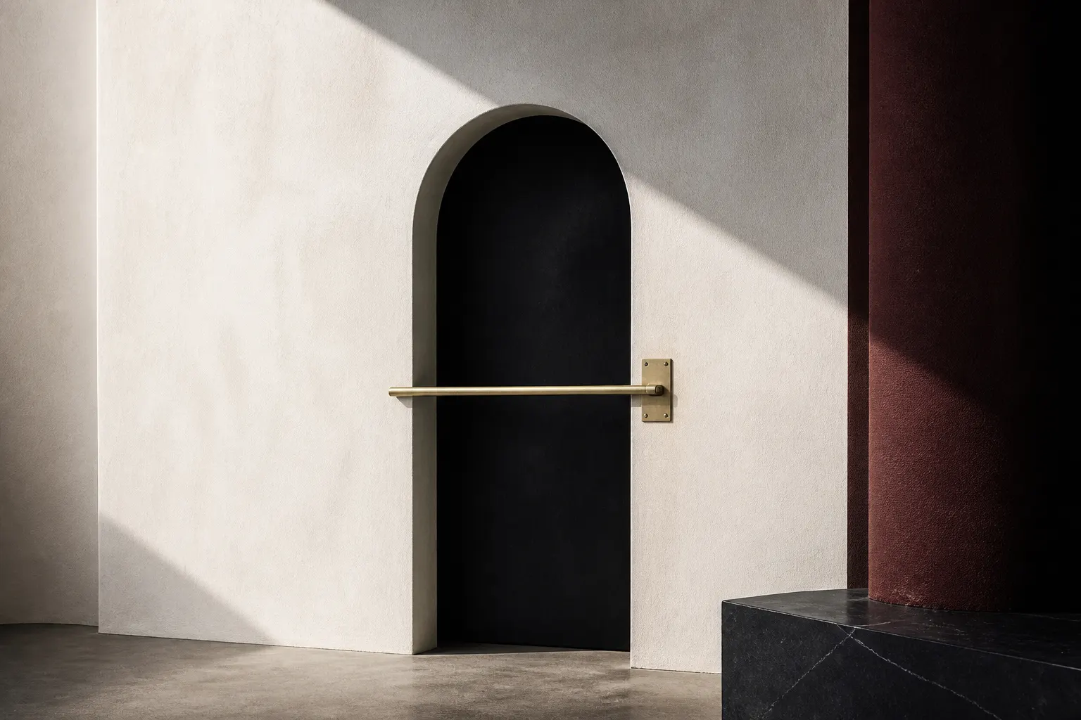 A black arched doorway in a plaster wall barred by a horizontal brass rod beside a burgundy column.